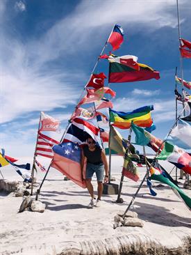 The picture shows a young man on the beach surrounded by national flags.